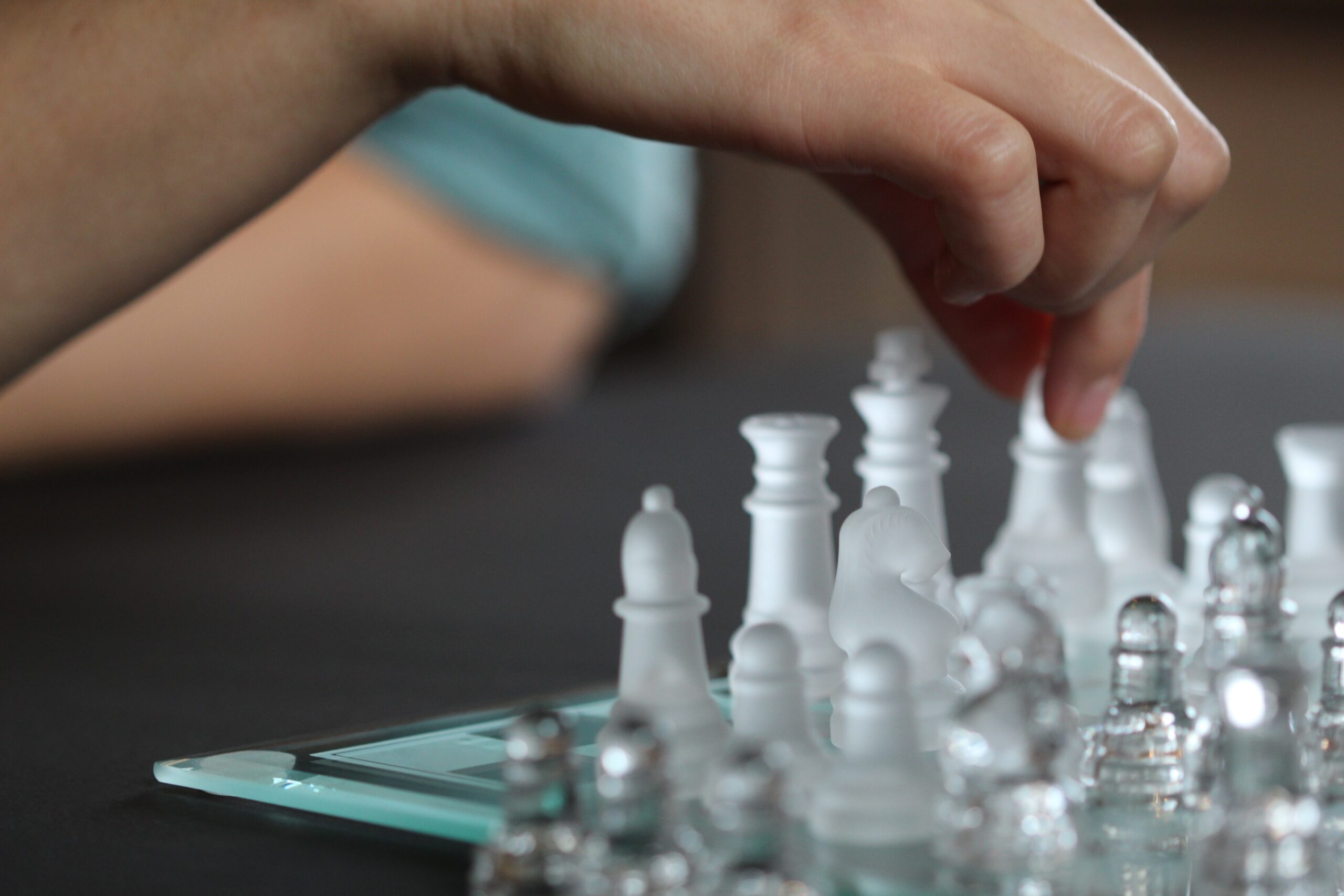 anne-nygard-Glass chess set hand in closeup moving piece-unsplash