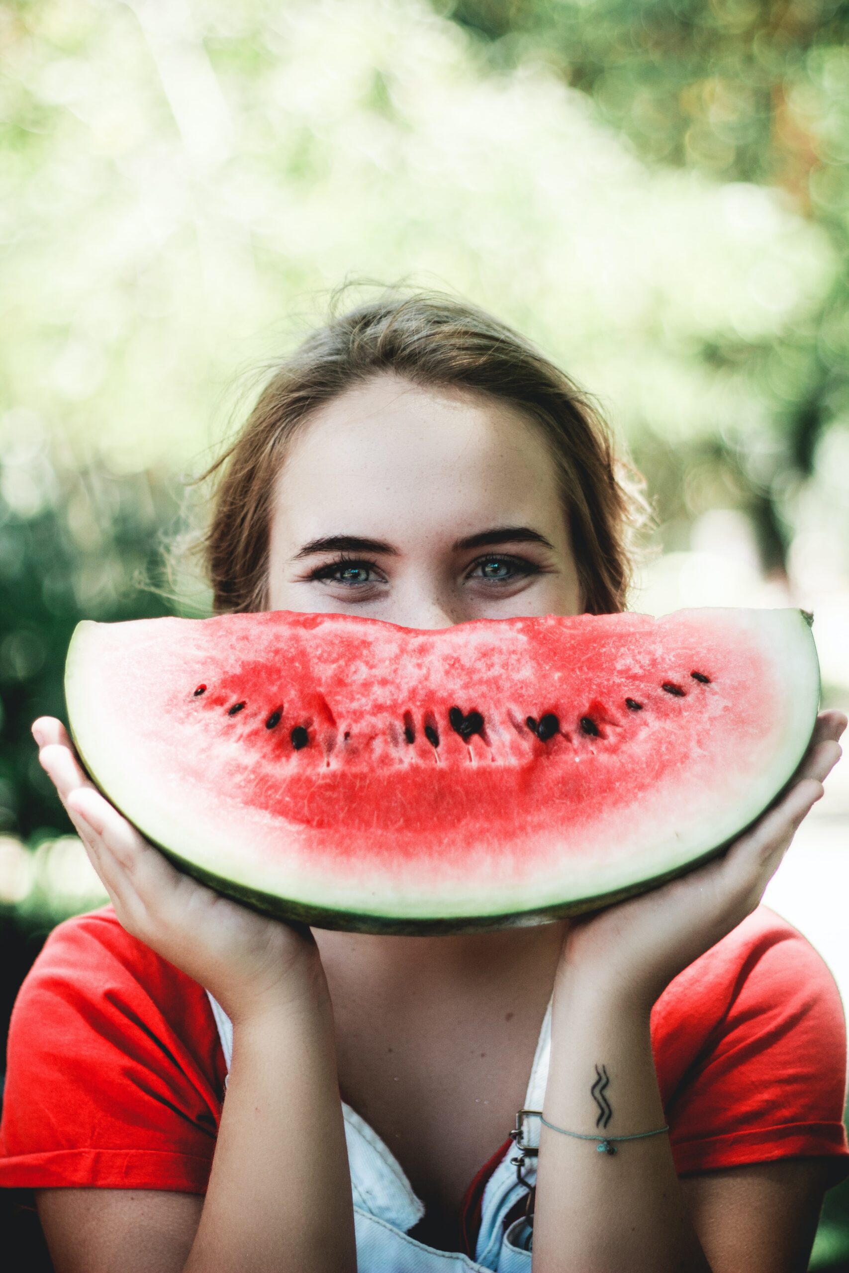 caju-gomes-young woman holding watermelon half in front of mouth-unsplash