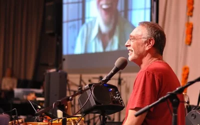 Krishna Das harmonium close-up during live kirtan performance, fingers poised for chant