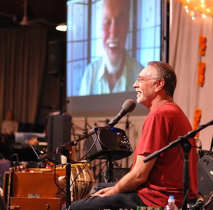 Krishna Das harmonium close-up during live kirtan performance, fingers poised for chant