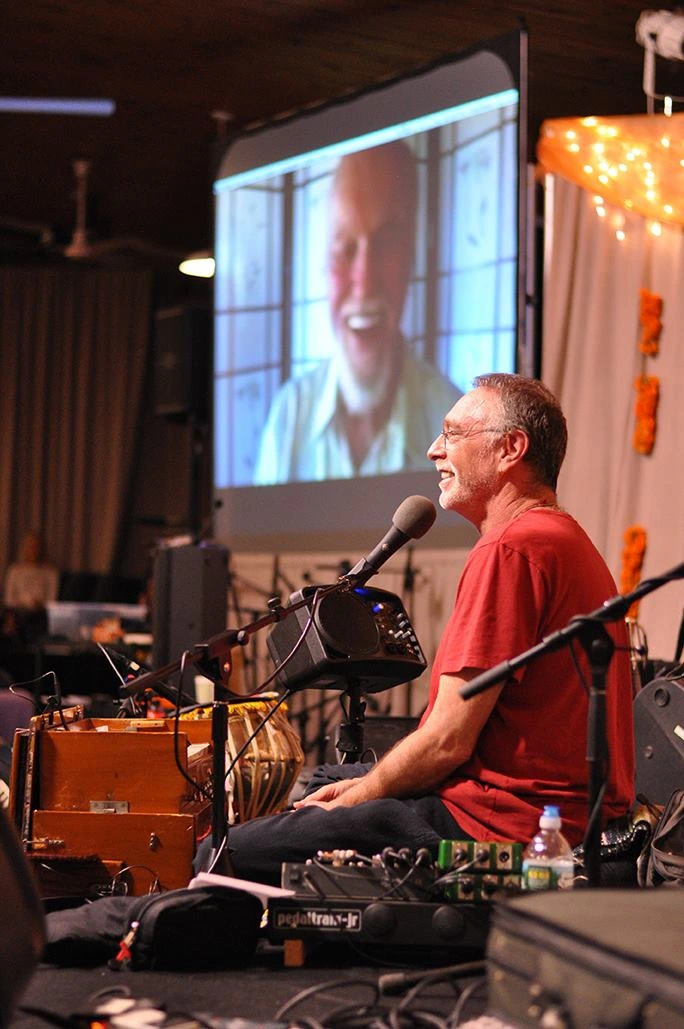 Krishna Das harmonium close-up during live kirtan performance, fingers poised for chant