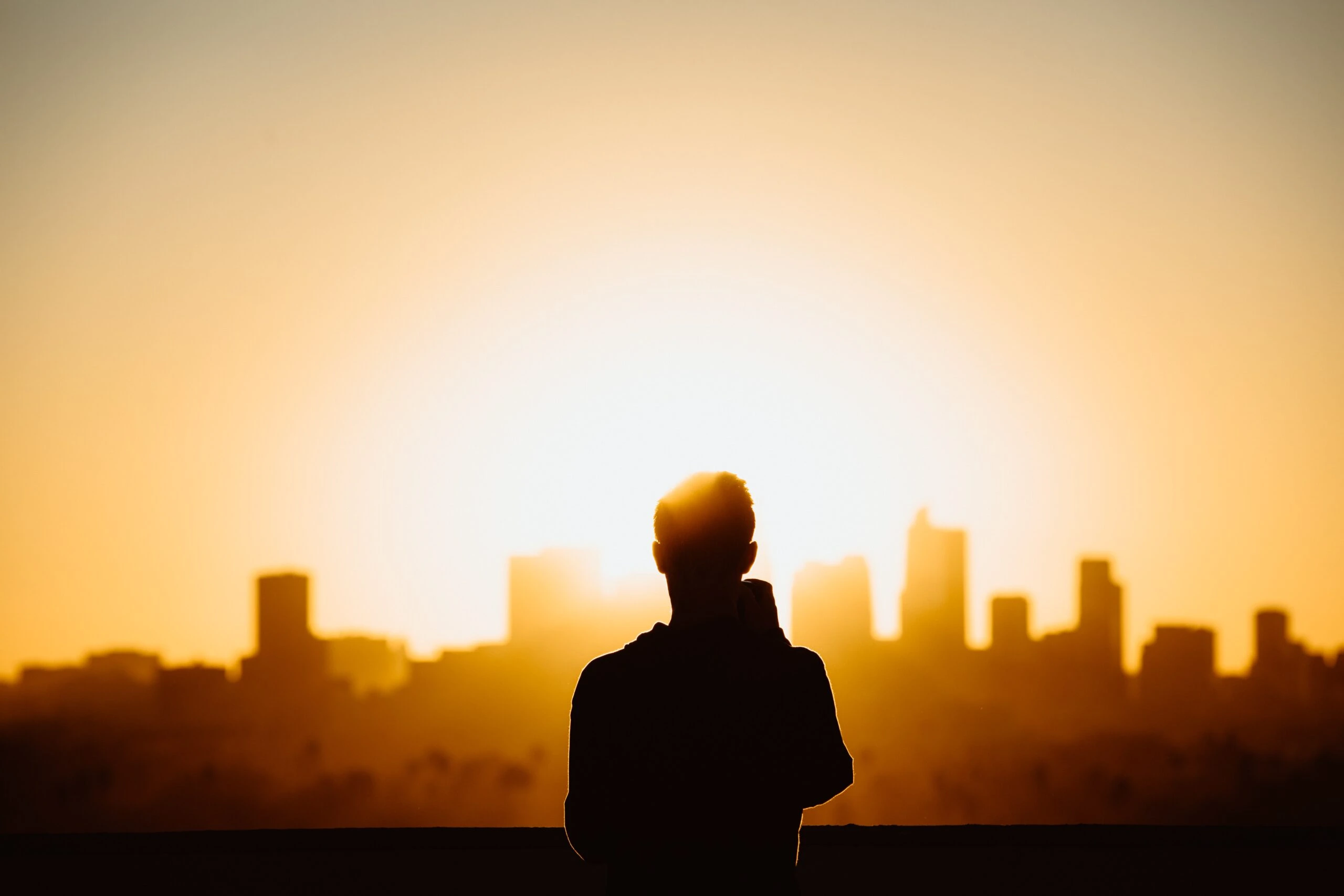 nathan-dumlao-lot-man drinking coffee at sunrise with city in foreground full morning light-unsplash-scaled